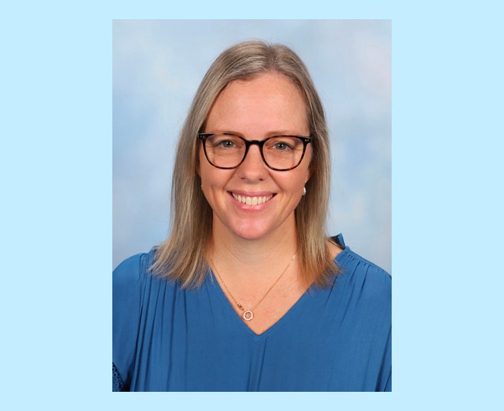 A woman smiling at the camera wearing glasses and a blue blouse.
