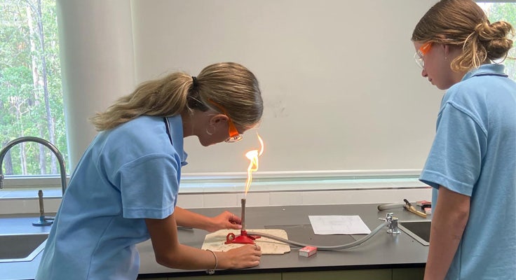 Two students in the Science room operating a bunsen burner which has a yellow flame.