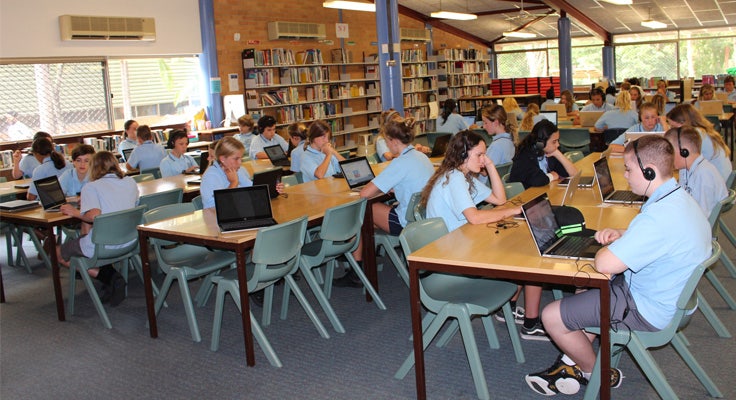 A group of students earing headphones and working on laptops in the Library.