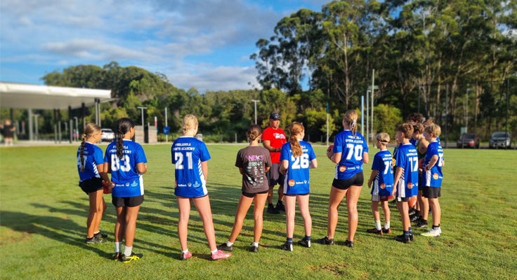 A group of students listening to a coach on a sport field.