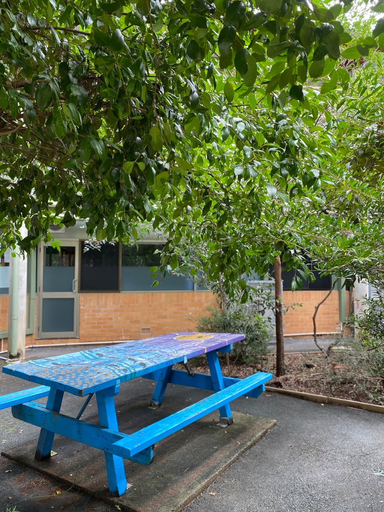 A blue painted table beneath a lilly pilly tree