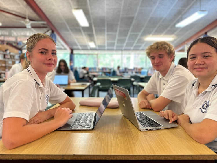 Three students sitting in the library with laptops in fron of them