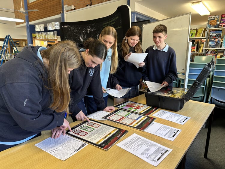 5 students leaning over a desk reading information flyers on desk