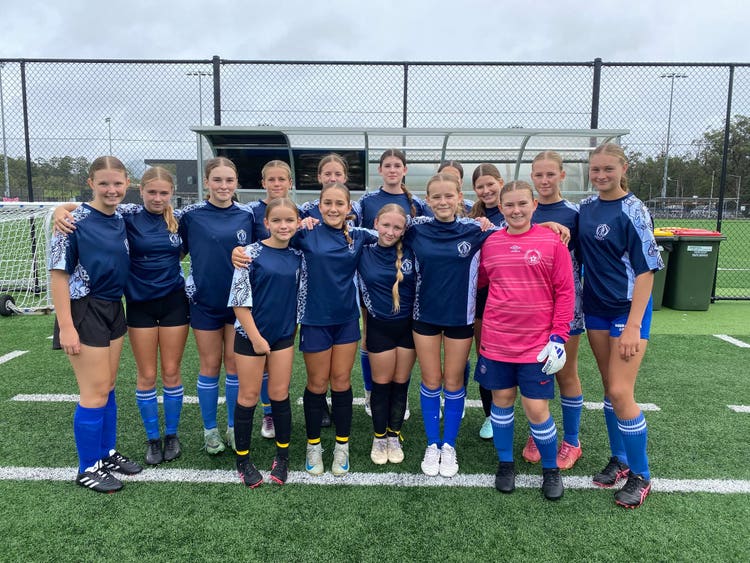 A team of girls in a soccer team standing together on a soccer field