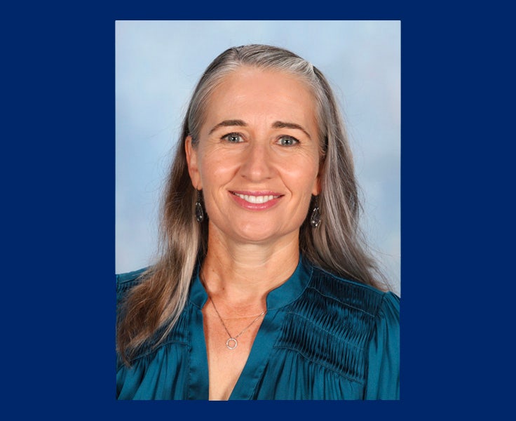 A woman smiling and wearing a shiny turquoise blouse.