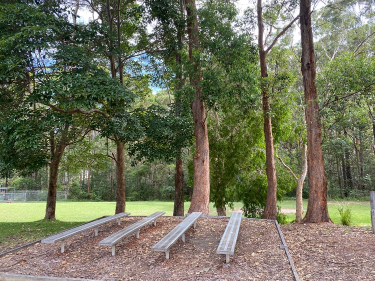 4 aluminium bench seats in front of trees with a green playground below