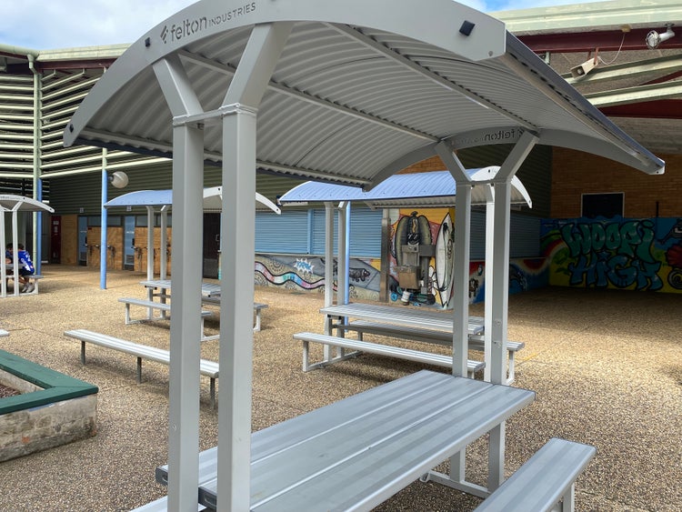Curved roof aluminium seats in front of a school canteen.